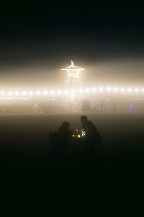 Free Silhouetted people at night with glowing lights in dense fog creating a mysterious atmosphere. Stock Photo