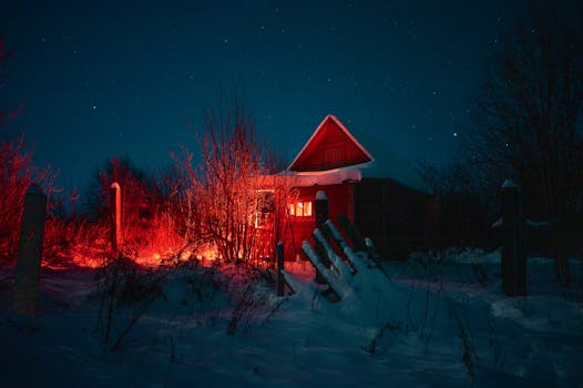 A snow-covered cabin emits a warm glow against a starry night sky, surrounded by winter scenery.