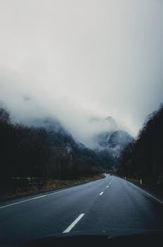 Empty scenic road leading to fog-covered mountains, creating a moody winter atmosphere.