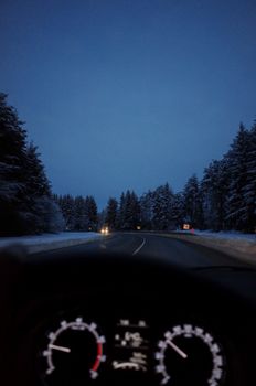 A winter evening drive through a snowy forest with headlights illuminating the road.