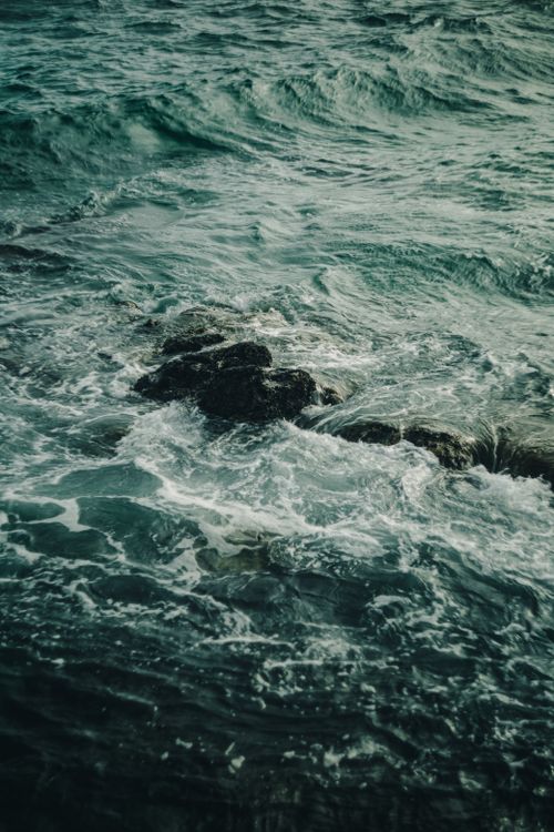 Free Captivating view of powerful ocean waves crashing against rugged rocks in moody lighting. Stock Photo