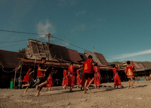 Free Men performing a traditional dance in a rural village, dressed in vibrant red attire under a clear sky. Stock Photo