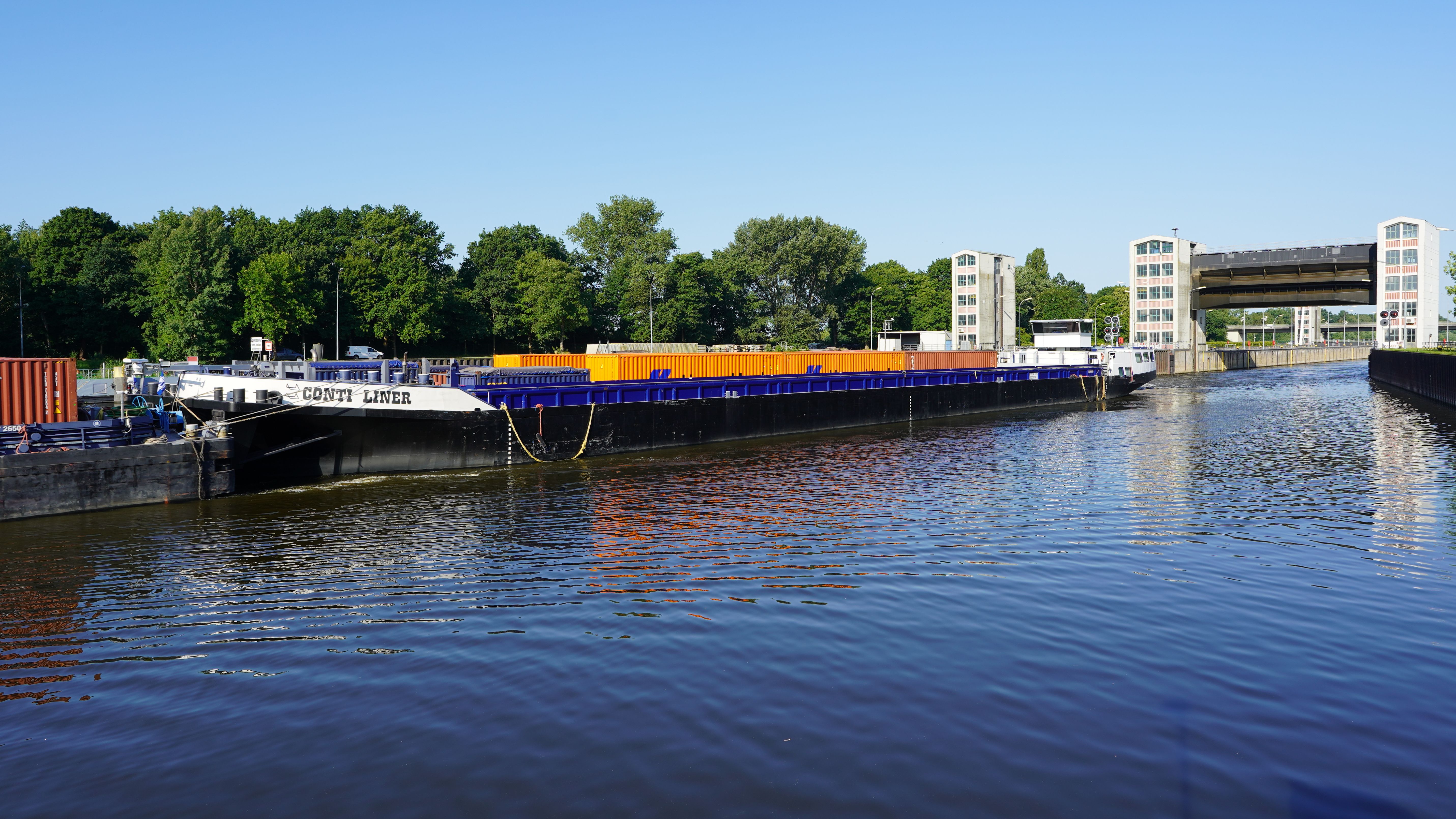 A cargo ship navigates Geesthacht's floodgate on a clear day, showcasing freight transport on the Elbe.