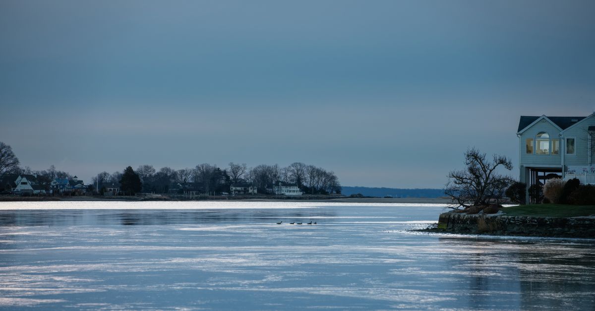 A serene winter shoreline scene at twilight with a charming house on the right.