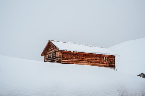 Free A solitary wooden cabin nestled in deep snow, creating a serene winter landscape. Stock Photo