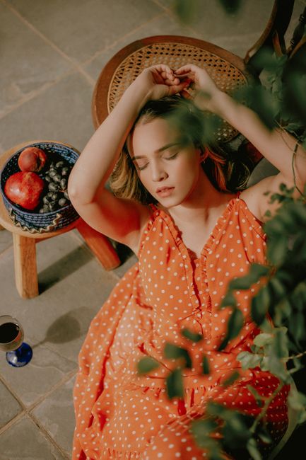 A woman in a polka dot dress resting comfortably, surrounded by fruit and plants, radiating tranquility and summer vibes.