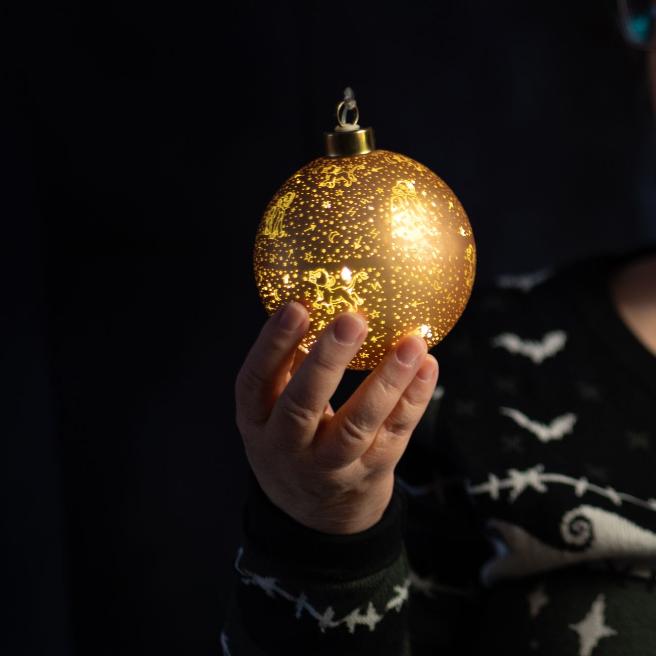 A hand holds a glowing ornamental bauble against a dark background, creating a festive mood.
