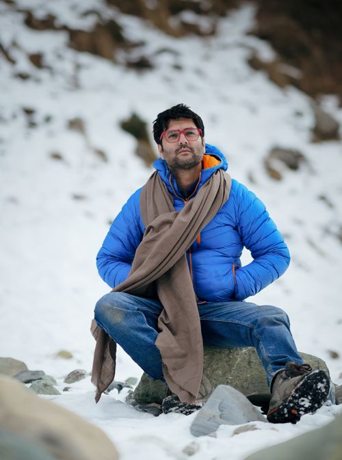 Free A man in a blue jacket sits on a rock in snowy Jammu and Kashmir. Stock Photo