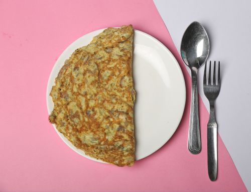 Free A tasty omelet served on a white plate with a fork and spoon on a pink background. Stock Photo