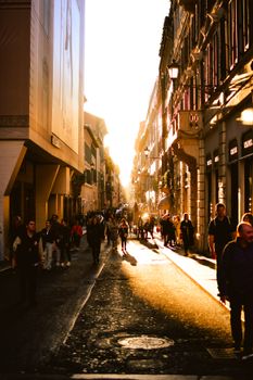 A vibrant city street scene captured at sunset with people walking along a sunlit avenue in Europe.