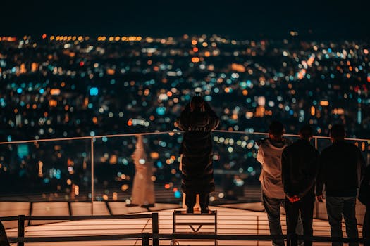A group overlooking a vibrant nighttime cityscape from a rooftop in Shibuya, Tokyo.