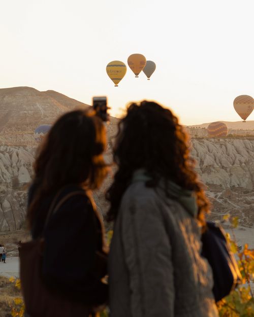 Free Silhouetted tourists view hot air balloons over Cappadocia's unique landscape during sunrise. Stock Photo