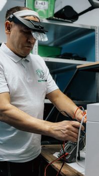 Technician uses magnifier loupes for precise electronic device repair in workshop.