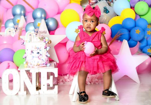 Adorable baby girl in a pink dress at a unicorn-themed first birthday party.