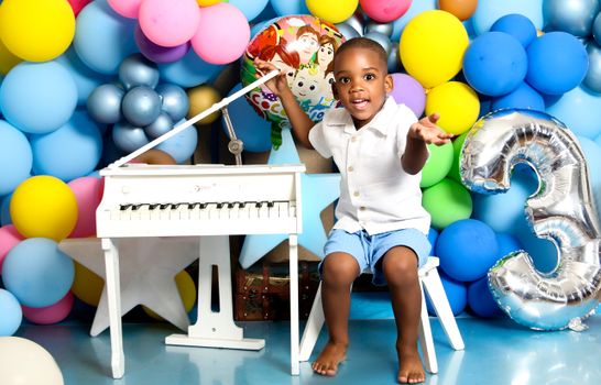 Joyful child at a birthday party surrounded by colorful balloons and a toy piano.