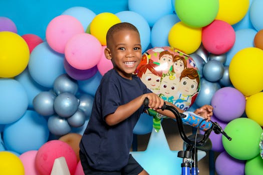 Joyful child on a bike at a vibrant birthday party with colorful balloons.