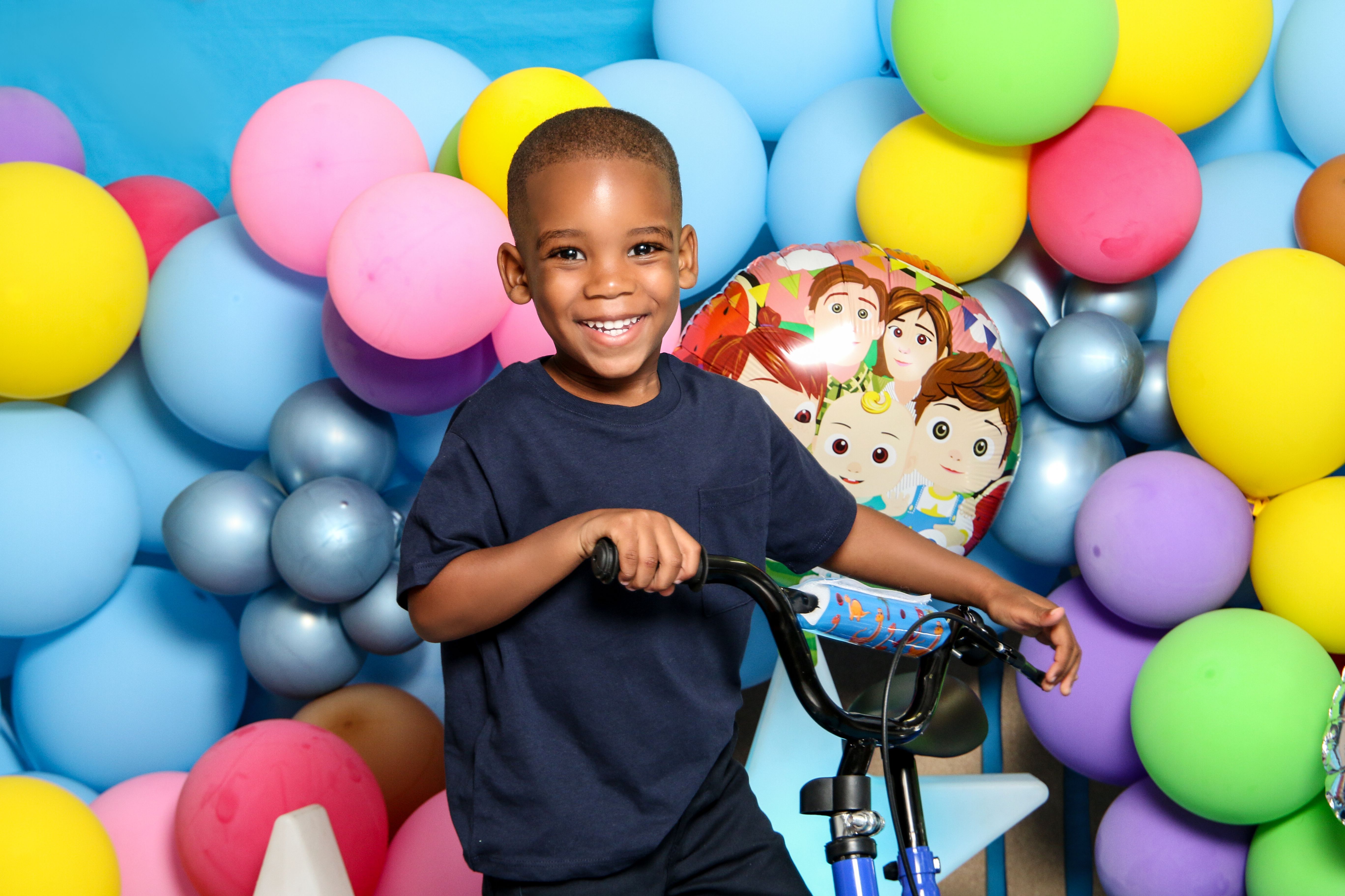 Smiling child poses with bicycle amidst colorful balloons at a birthday party