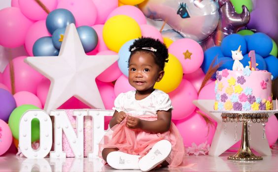 Cute baby celebrates first birthday with balloons, cake, and decorations.