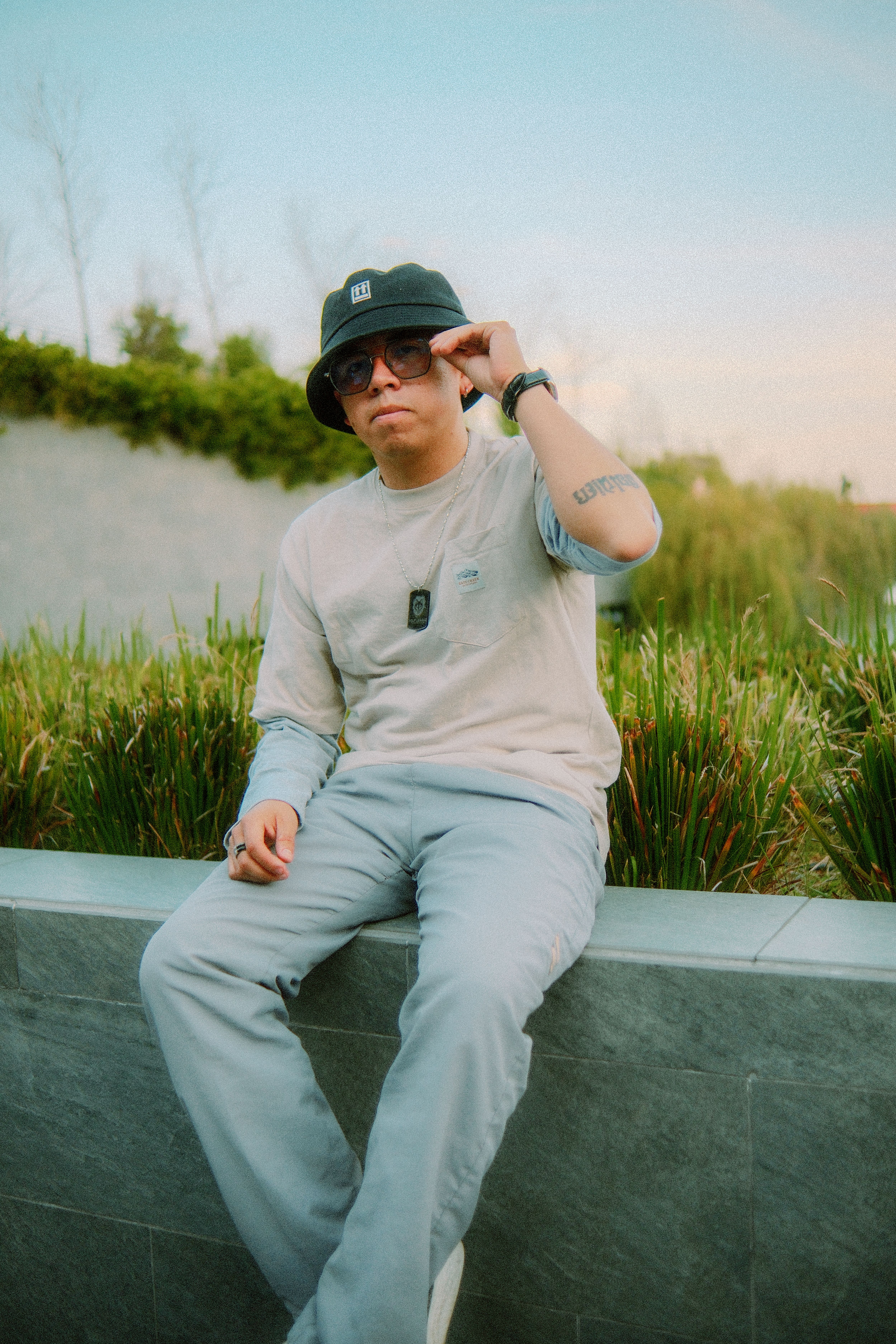 Stylish man wearing casual outfit sits on concrete ledge in urban park.