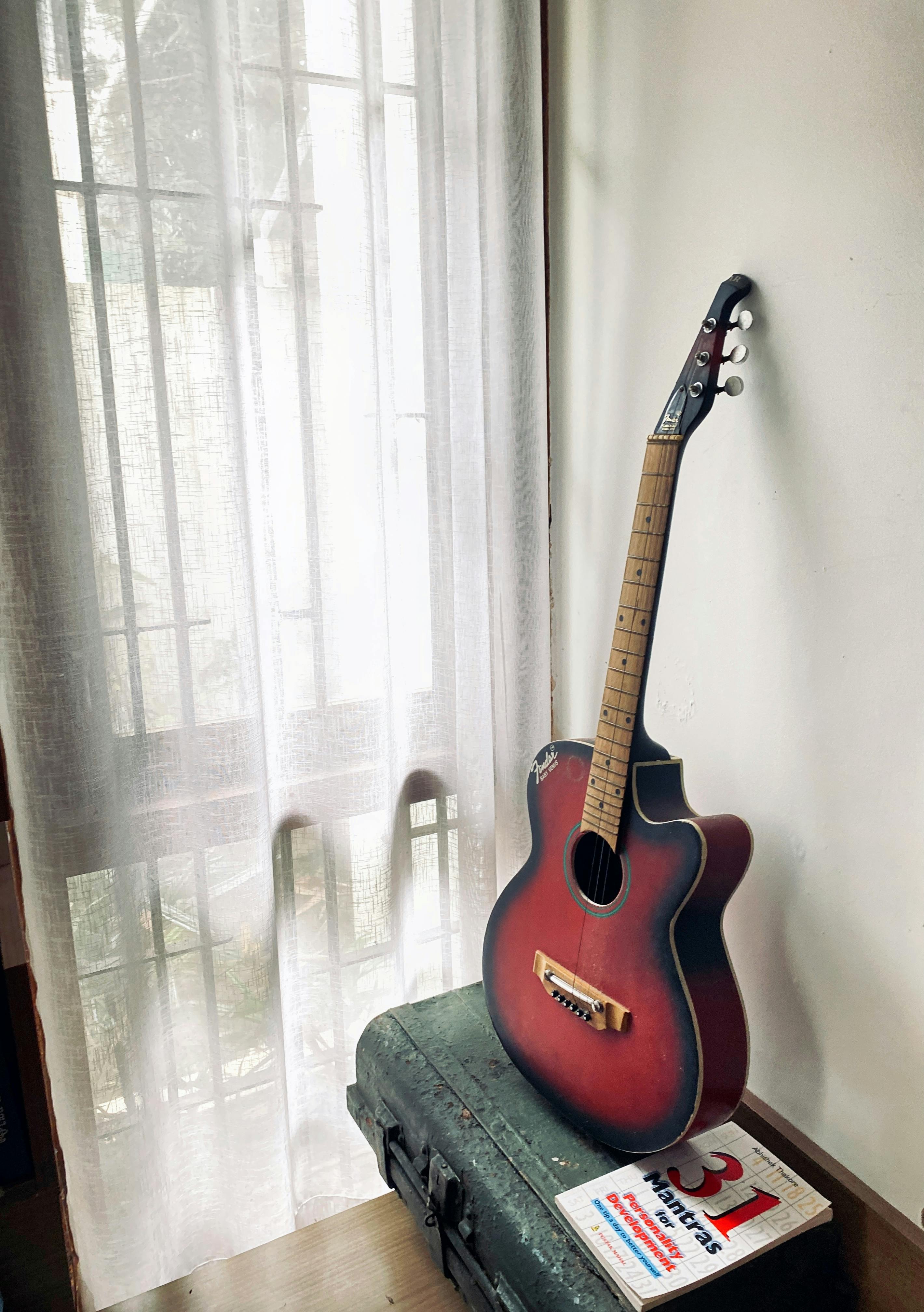 무료 창문에 기대어 놓인 어쿠스틱 기타와 기어 케이스 위의 책 옆. 스톡 사진