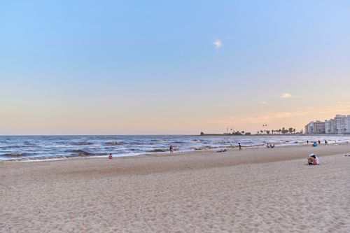 Free Sunset view of a tranquil beach with distant city skyline enhancing the peaceful ambiance. Stock Photo