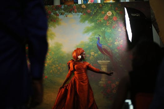 A model in an orange dress poses gracefully in front of a vibrant peacock backdrop in a studio setting.