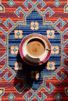 Artistic flat lay of a coffee cup on a colorful, geometric-patterned carpet.