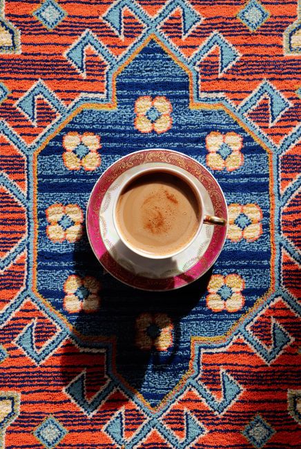 Artistic flat lay of a coffee cup on a colorful, geometric-patterned carpet.