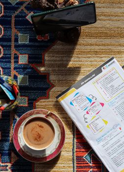 A warm, inviting workspace with coffee, colorful notebook, and decorative carpet, perfect for study or creative work.