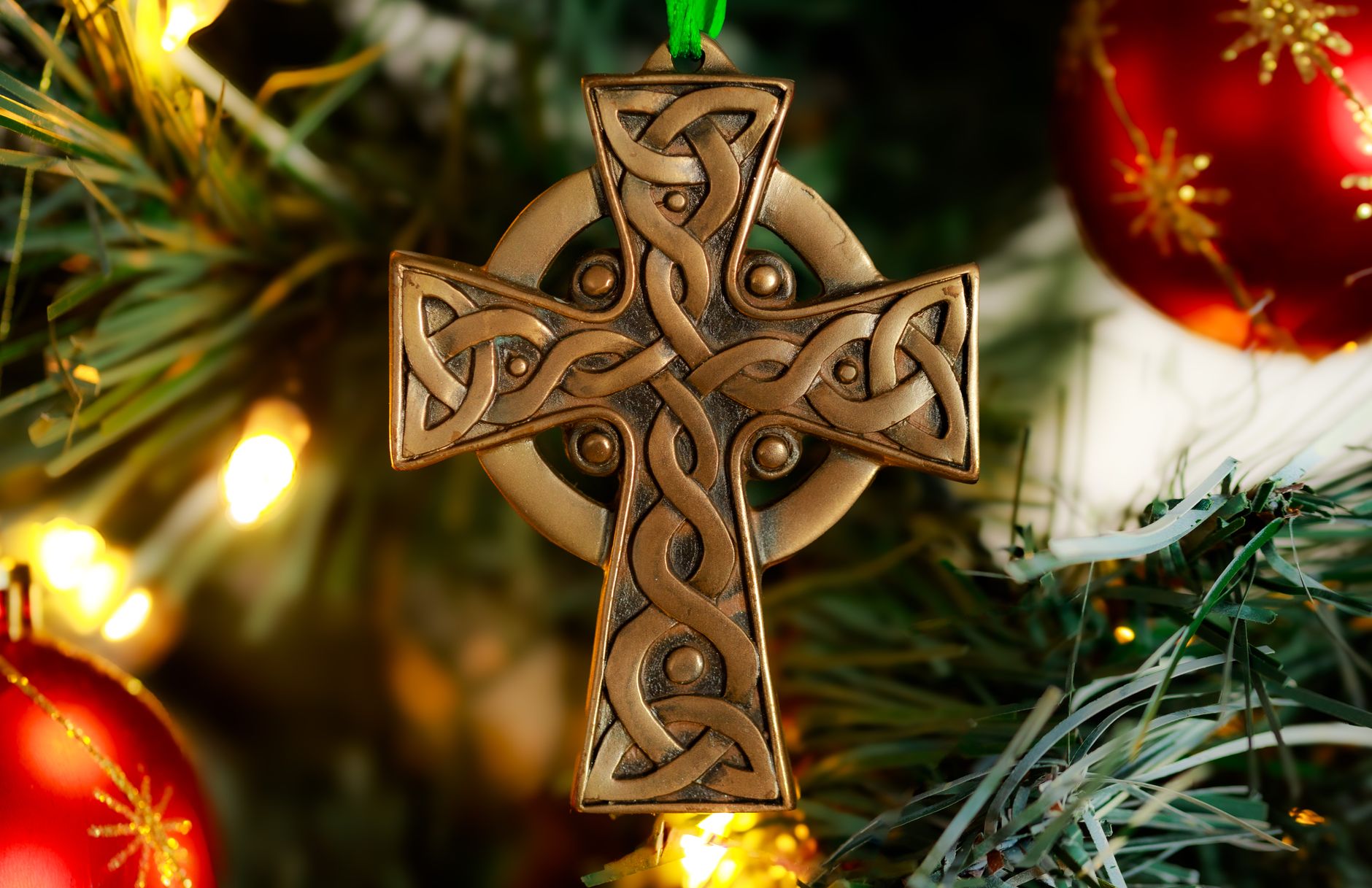 Elegant Celtic cross ornament hanging on a Christmas tree with festive decorations.