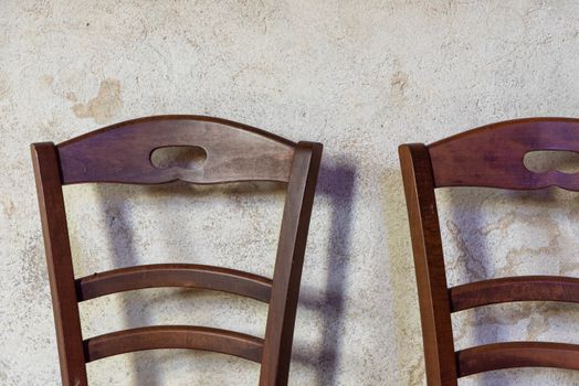 Two wooden chairs with curved backs against a rustic textured wall, capturing a minimalist aesthetic.