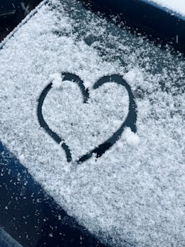 A heart shape drawn on a snow-covered car window, capturing winter's charm.