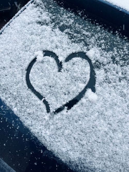 Free A heart shape drawn on a snow-covered car window, capturing winter's charm. Stock Photo
