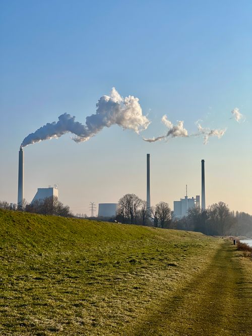 Free Industrial chimneys with smoke emissions under a clear blue sky in a rural setting. Stock Photo