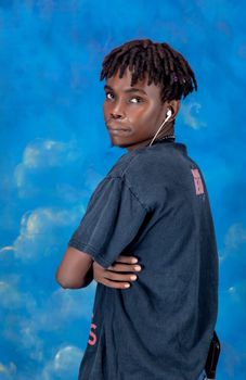 A portrait of a young man with earphones, posing against a vibrant blue backdrop.