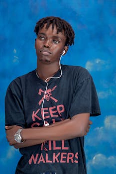 Casual portrait of a young man in a black T-shirt with headphones against a blue background.