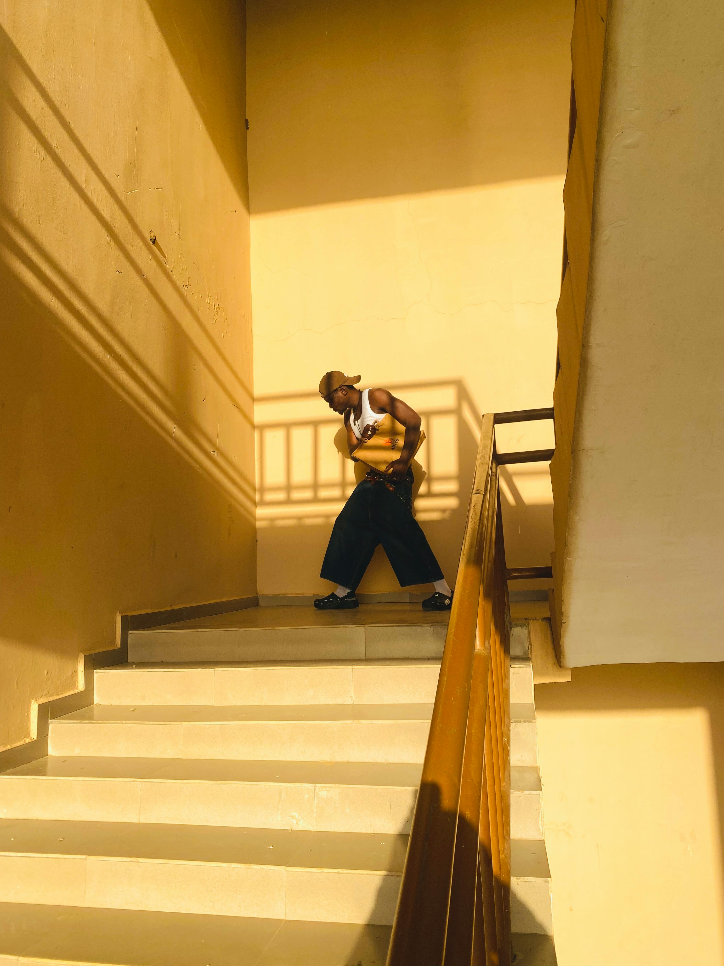 Gratis Una persona a la moda posa en una escalera iluminada por el sol, mostrando un estilo urbano moderno. Foto de stock