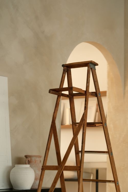 Free Vintage wooden ladder in a minimalist studio setting with ceramic vases and textured walls. Stock Photo
