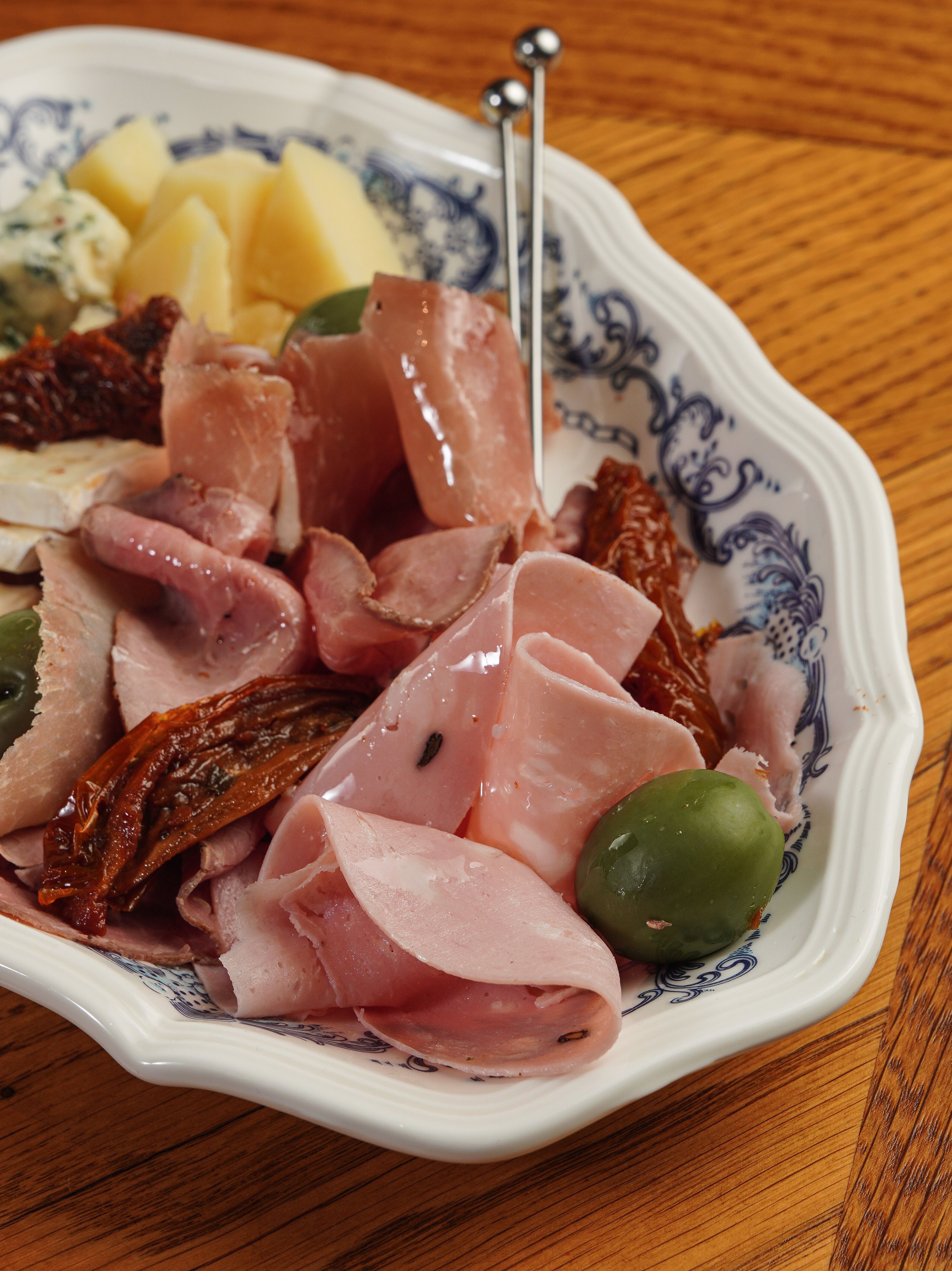 A platter of sliced salami and provolone pinwheels showing the spiral layers of tortilla, cream cheese spread, salami, and provolone, with a few whole rolled tortilla logs in the background.