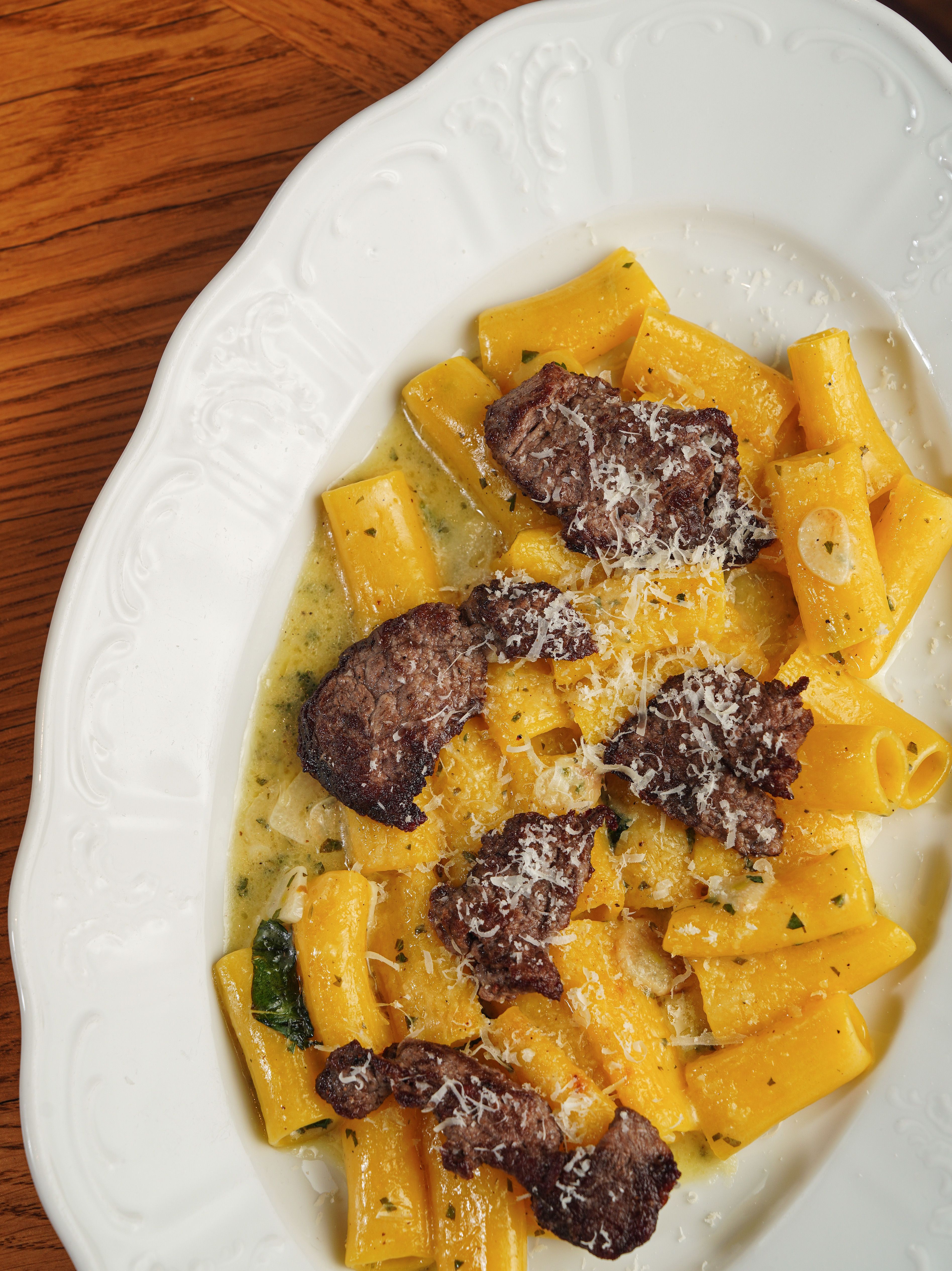 Rigatoni pasta with savory beef slices and cheese served on a white plate.