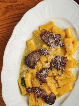 Rigatoni pasta with savory beef slices and cheese served on a white plate.