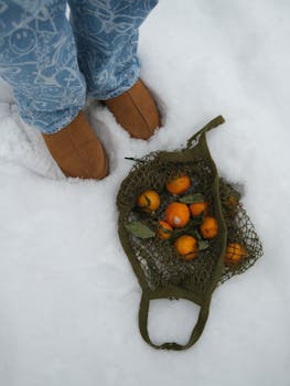 A mesh bag of persimmons rests on snow, paired with brown boots.