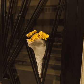 Artistic bouquet of yellow flowers resting in an iron gate, creating a moody urban feel.