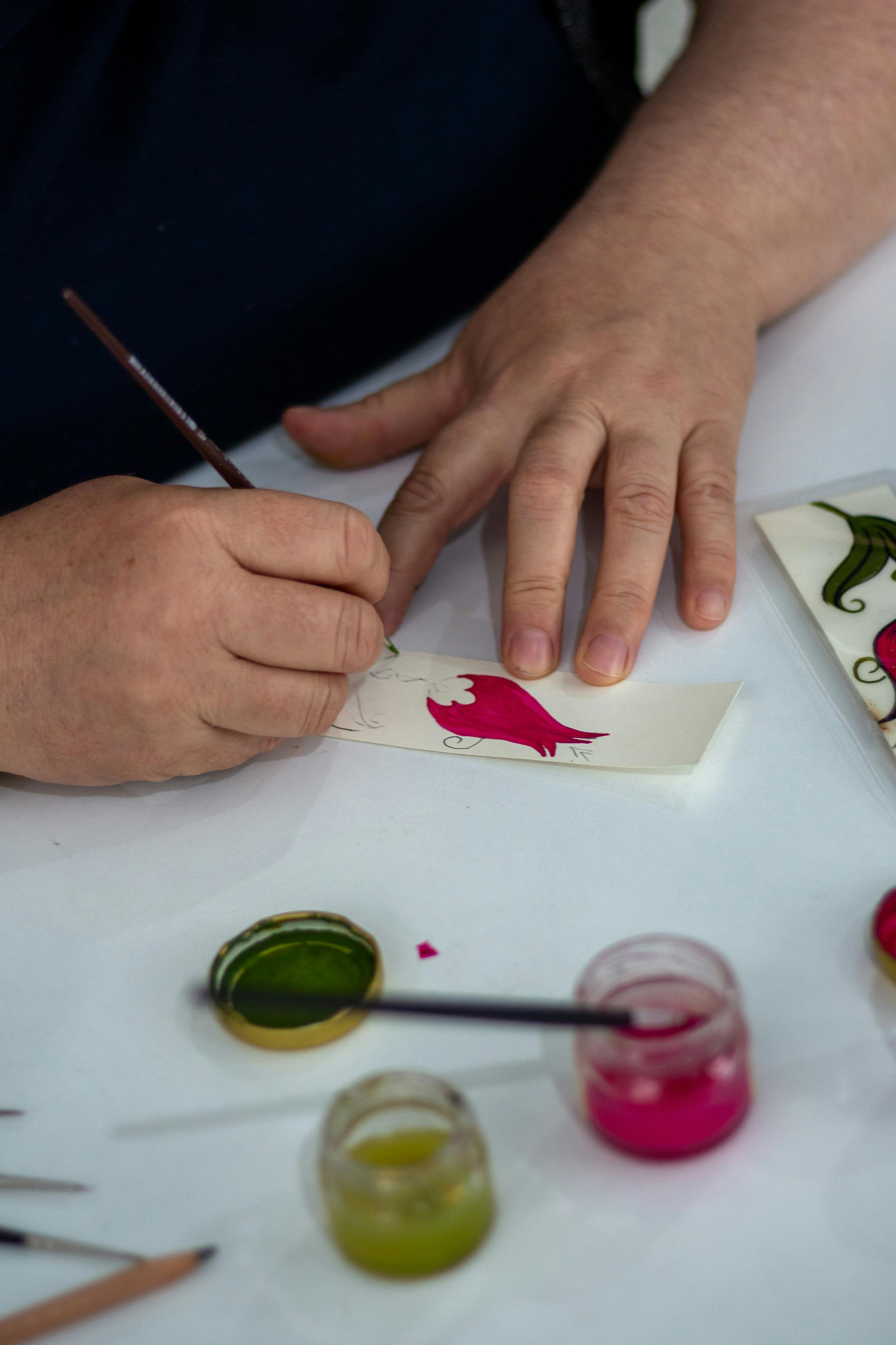 Close-up of artisan hand painting designs with brush and inks on paper.