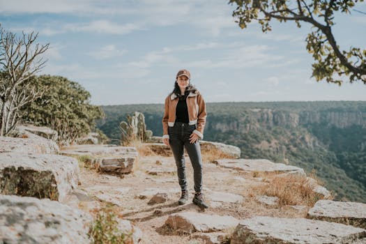 A woman stands on a rocky clifftop, showcasing the beauty of nature and adventure in a mountainous landscape.