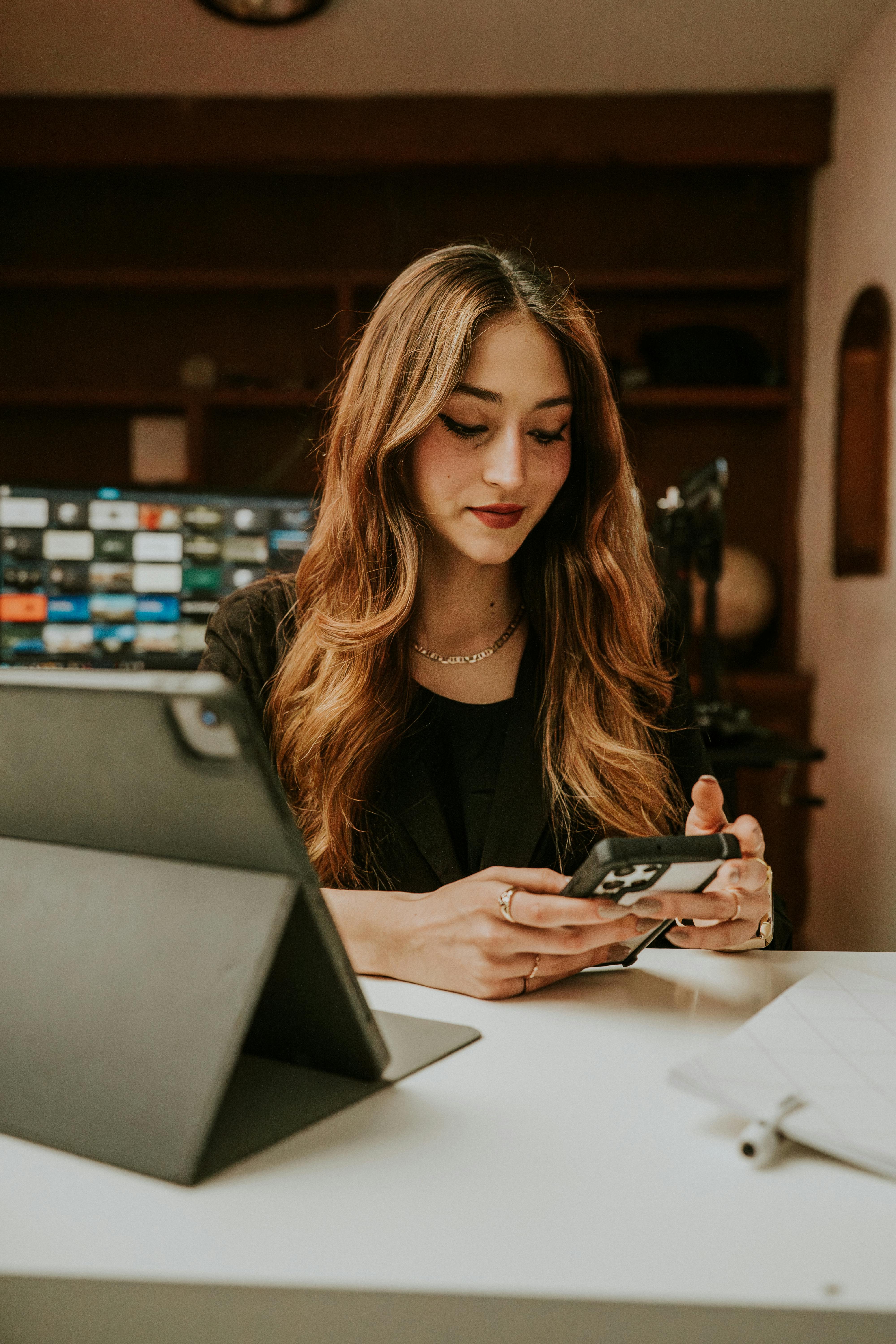 Gratis Mujer joven profesional trabajando con un teléfono inteligente en un acogedor entorno de oficina en casa. Foto de stock