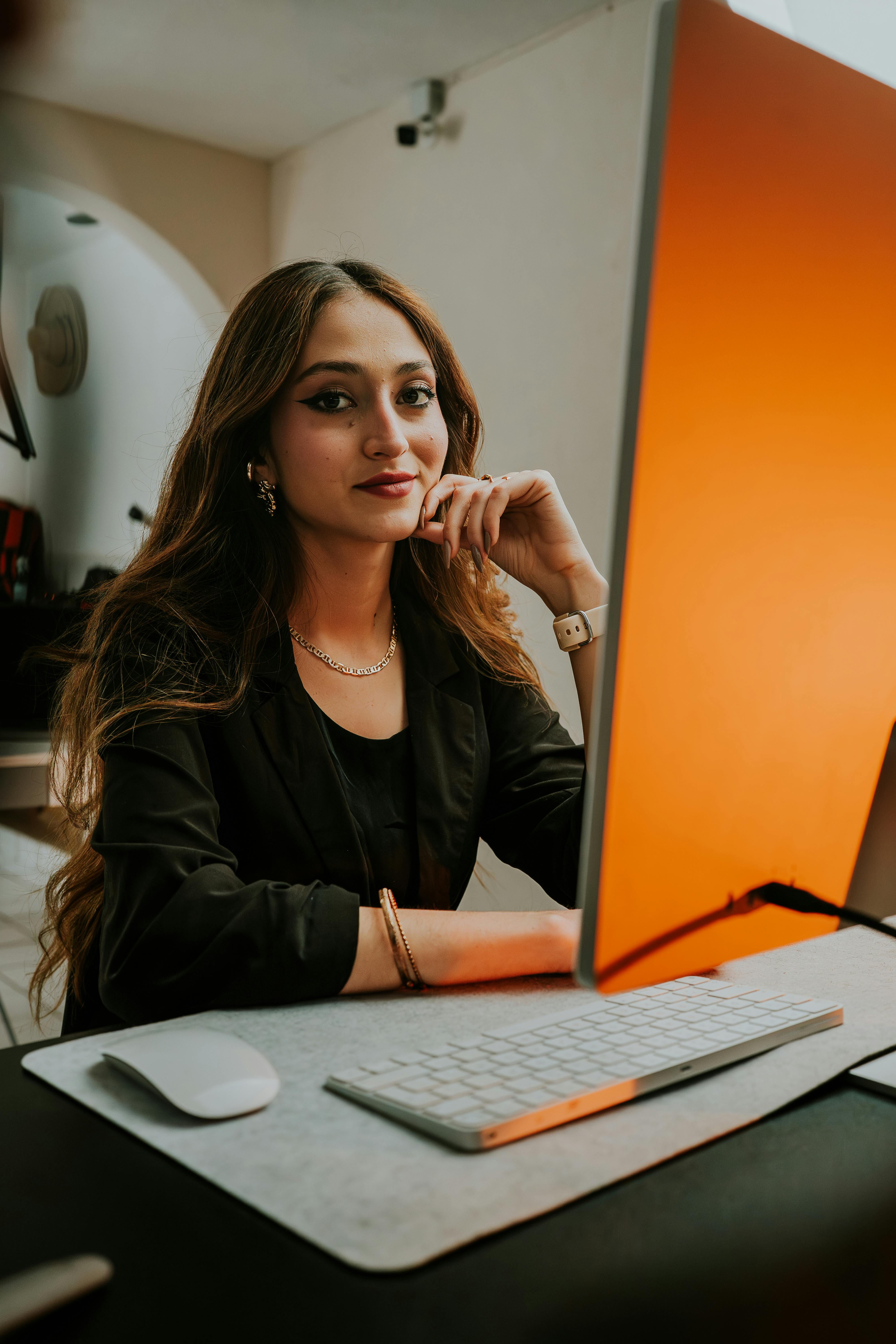 A confident young businesswoman working at a stylish desk setup with a vibrant computer screen.