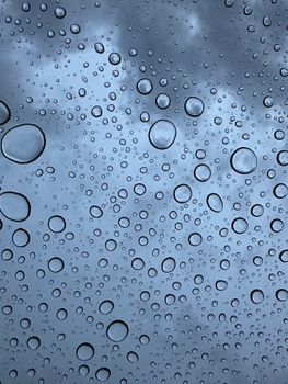 Raindrops on glass with a cloudy sky create a serene mood.