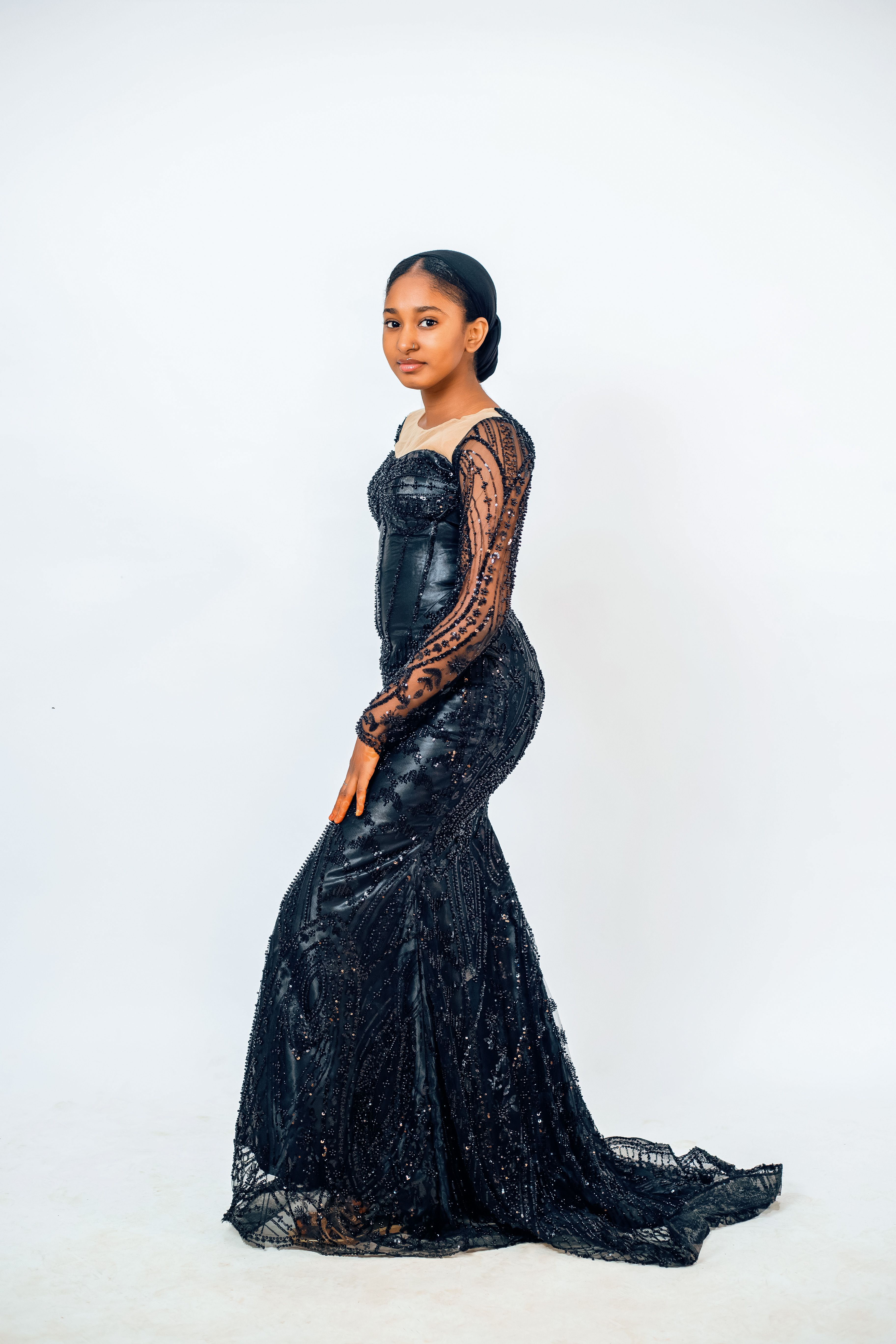 Elegant woman posing in a black sequin evening gown against a white backdrop.
