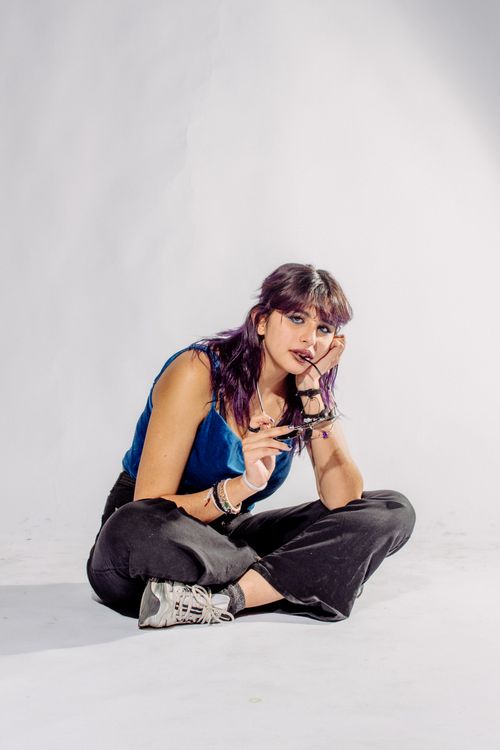Free Fashionable woman sitting casually on a studio floor. Captures modern style and relaxed mood. Stock Photo